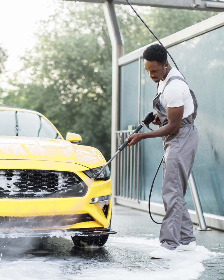 Man washing his luxury yellow car under high pressure water jet